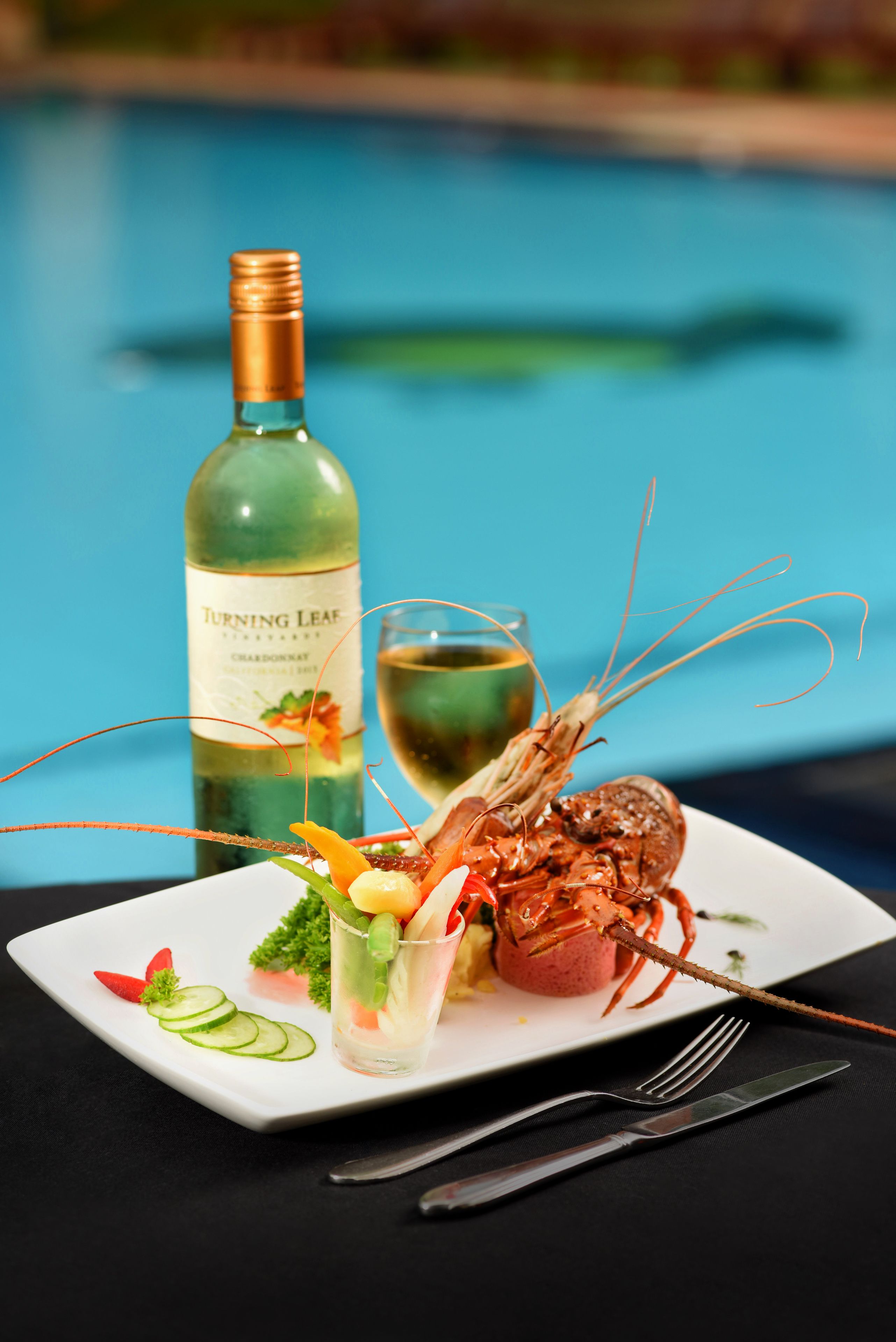 A seafood dish with a lobster tail, a glass of white wine, and a bottle of wine labeled "Turning Leaf" on a white plate.