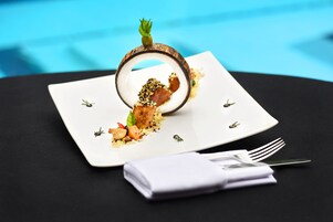 Un plato blanco con una presentación original de comida, que incluye carne, verduras y un adorno que recuerda a una cáscara de coco.