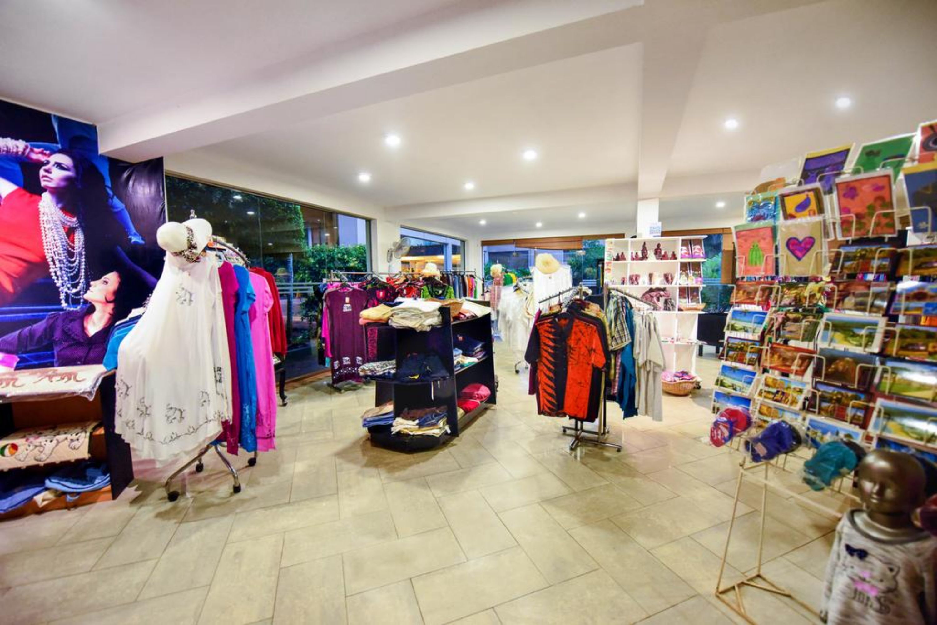Una tienda de ropa con perchas llenas de prendas, un maniquí y una exposición de postales.