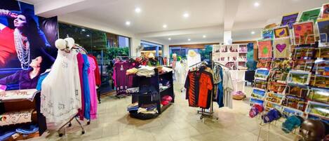 Una tienda de ropa con perchas llenas de prendas, un maniquí y una exposición de postales.