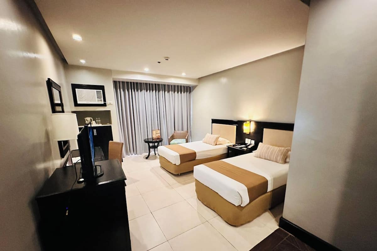 A hotel room with two beds, a desk, a chair, a TV, and a window with curtains.