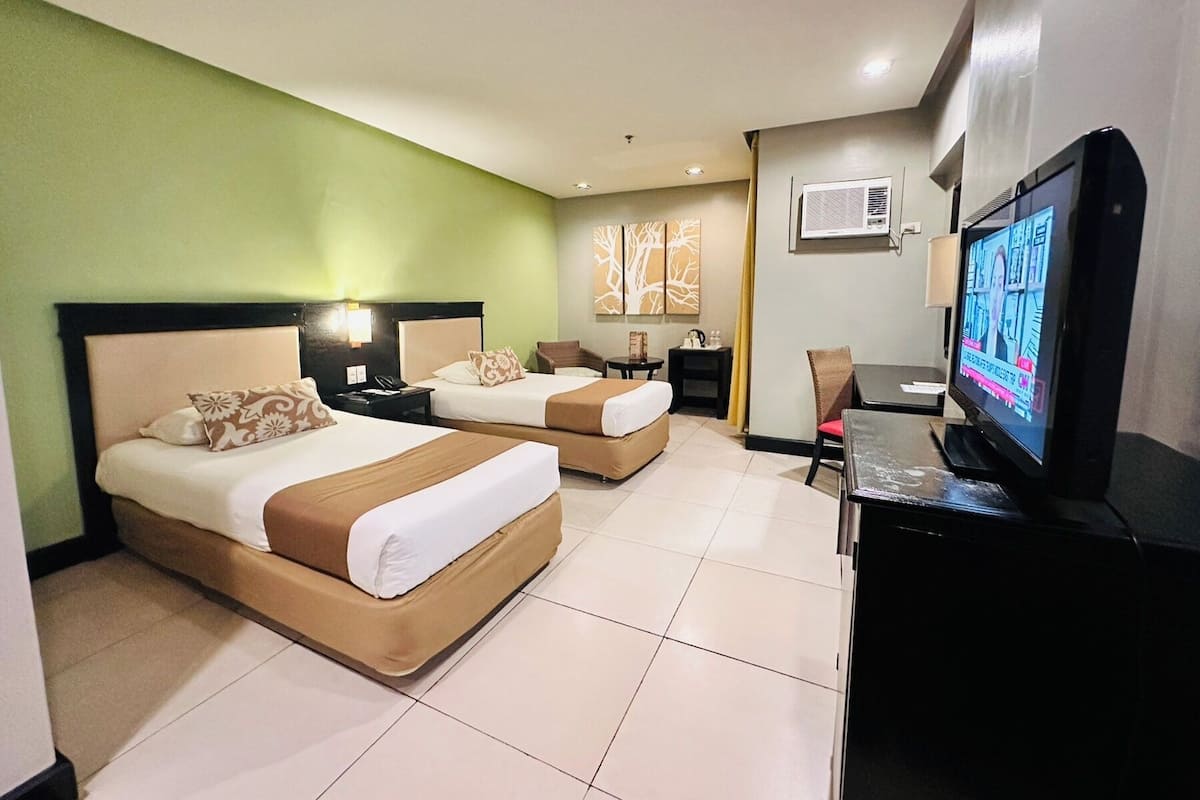 A hotel room with two beds, a desk, a chair, a television, and artwork on the walls.
