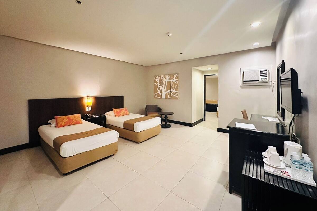 A hotel room with two beds, a desk with a chair, a TV, and a minibar.
