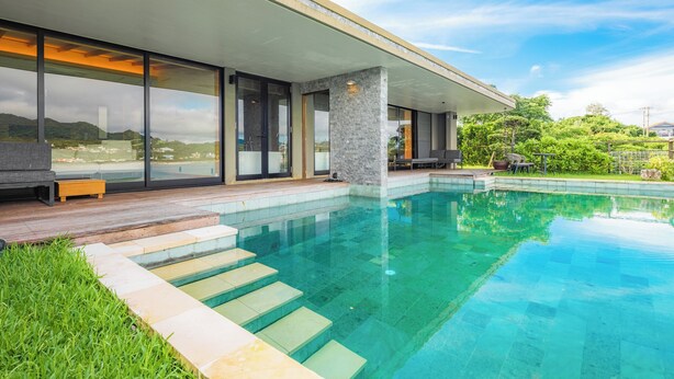 A modern house with a swimming pool, large windows, and a deck area. - Sesoko Sansui (Motobu)