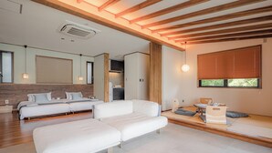 A modern hotel room with a large bed, a sofa, a dining area, and a kitchen in the background. - Sesoko Sansui (Motobu)