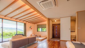 A modern hotel room with a wooden floor, a sofa, a bed, and a large window offering a view of the outdoors. - Sesoko Sansui (Motobu)