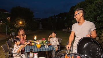 An outdoor dining area with a grill, table, chairs, and a lantern.