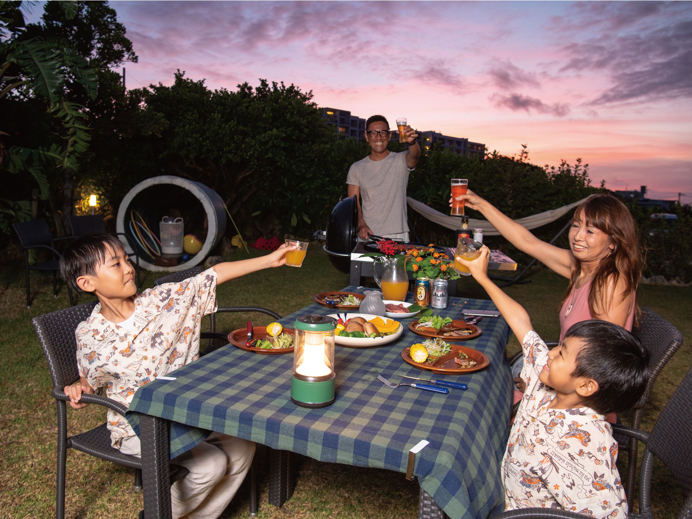 A group of people seated around a table with a checkered tablecloth, enjoying a meal outdoors at dusk.