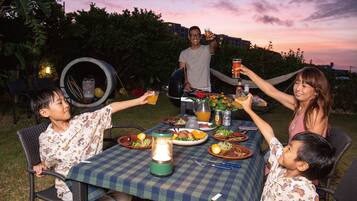 A group of people seated around a table with a checkered tablecloth, enjoying a meal outdoors at dusk.