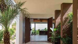A modern building entrance with a palm tree and potted plants. - Condominium T-Room (Yomitan)