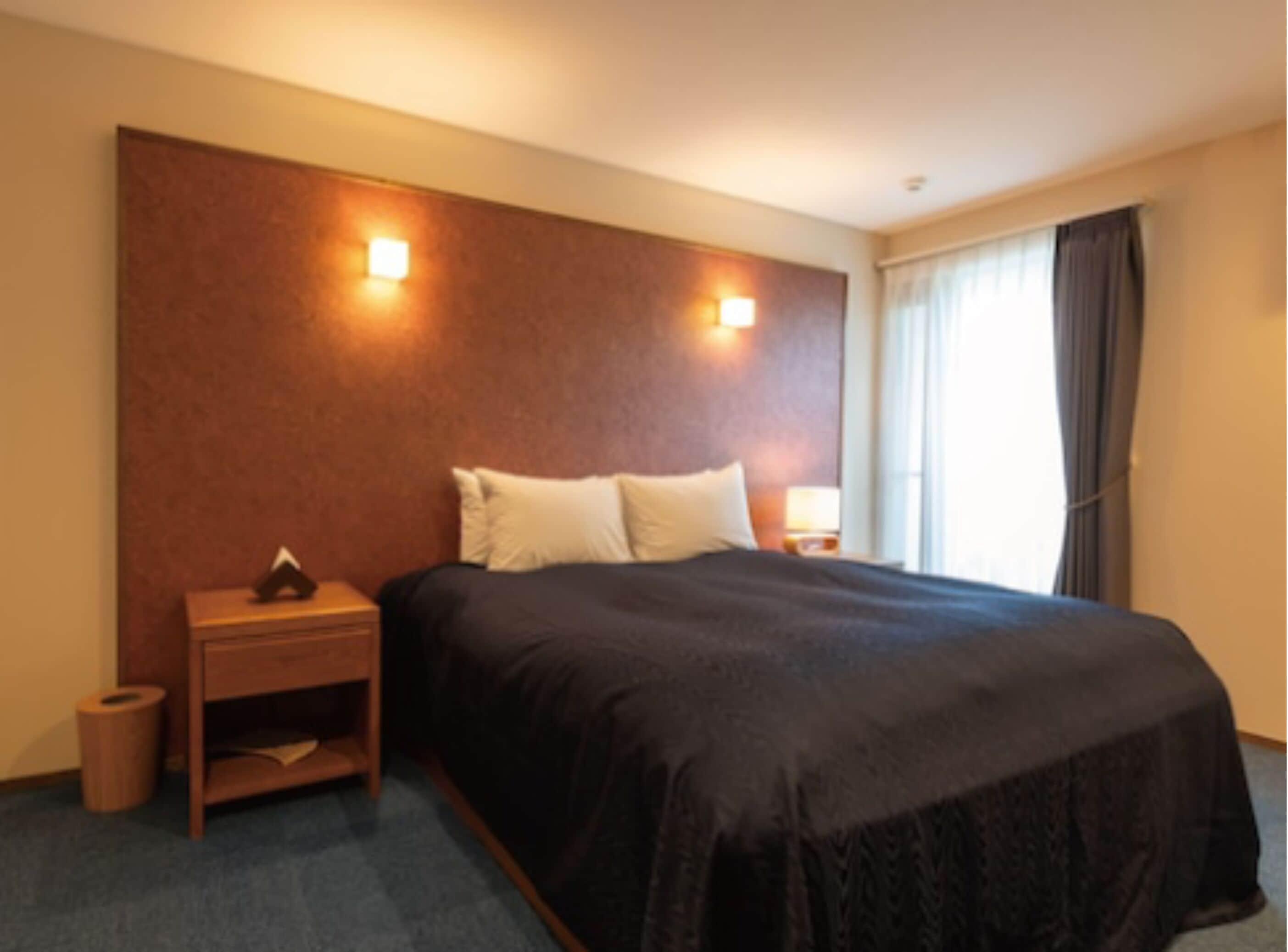 Une chambre d’hôtel avec un grand lit, deux tables de chevet, une petite table et une fenêtre avec des rideaux.