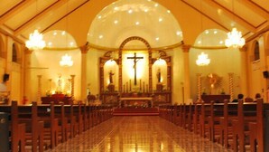 Interior de igreja com piso de mármore, bancos de madeira e altar central com uma cruz.