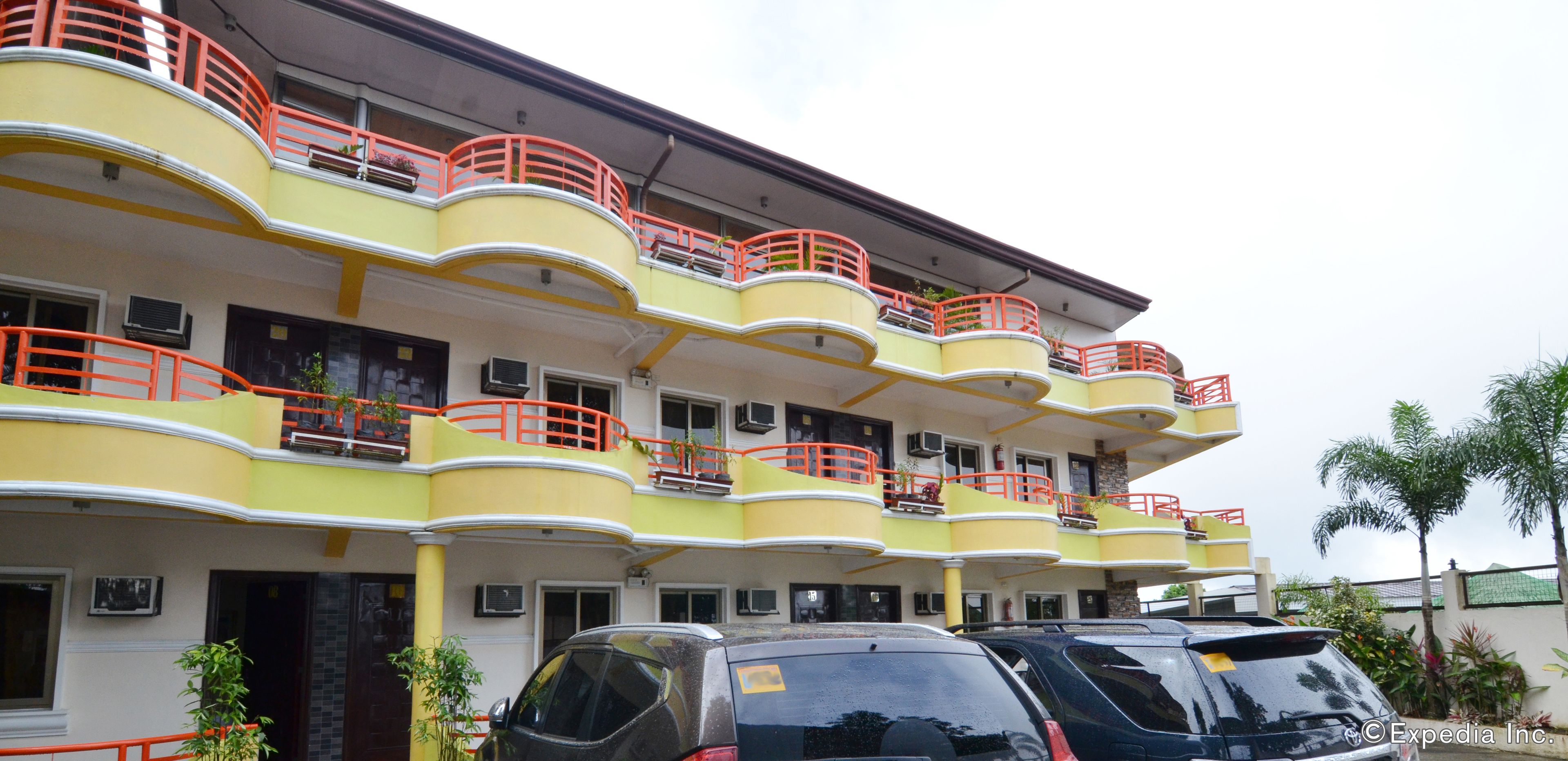 A multi-story hotel with balconies, air conditioning units, and parked cars.