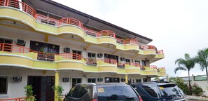 Un hôtel à plusieurs étages, doté de balcons, de climatiseurs et d’un parking.