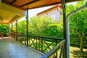 A covered outdoor area with a tiled floor, metal railing, and a view of a garden with trees and a building in the background. - Paradise Town Villa Hazel (Serik)