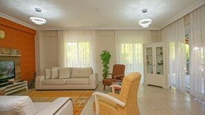 A living room with a beige sofa, a wicker chair, a television, and a cabinet with glass doors. - Paradise Town Villa Hazel (Serik)