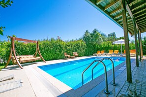 A swimming pool with lounge chairs and a swing chair, surrounded by greenery. - Paradise Town Villa Hazel (Serik)