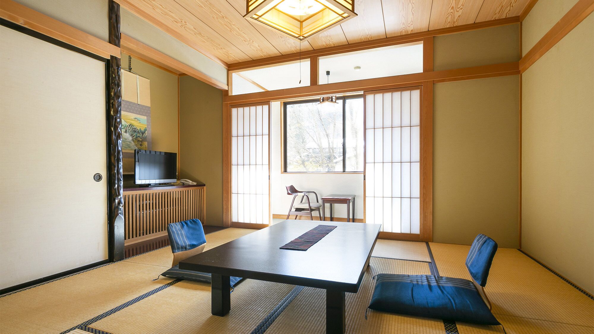 A traditional Japanese room with tatami flooring, a low table, and a television on a cabinet.