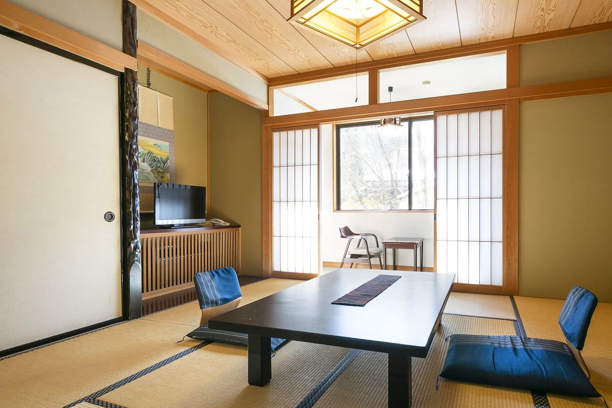 A traditional Japanese room with tatami flooring, a low table, and a television on a cabinet.