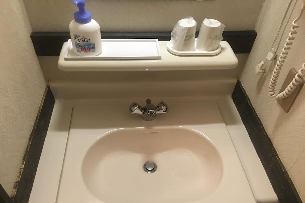 A bathroom sink with a mirror, a soap dispenser, and two toilet paper rolls on a holder.