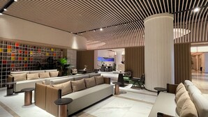 Un hall d’entrée spacieux au design moderne, comprenant un grand espace de détente avec des canapés et des tables, un mur décoratif orné de carreaux colorés et une grande colonne.