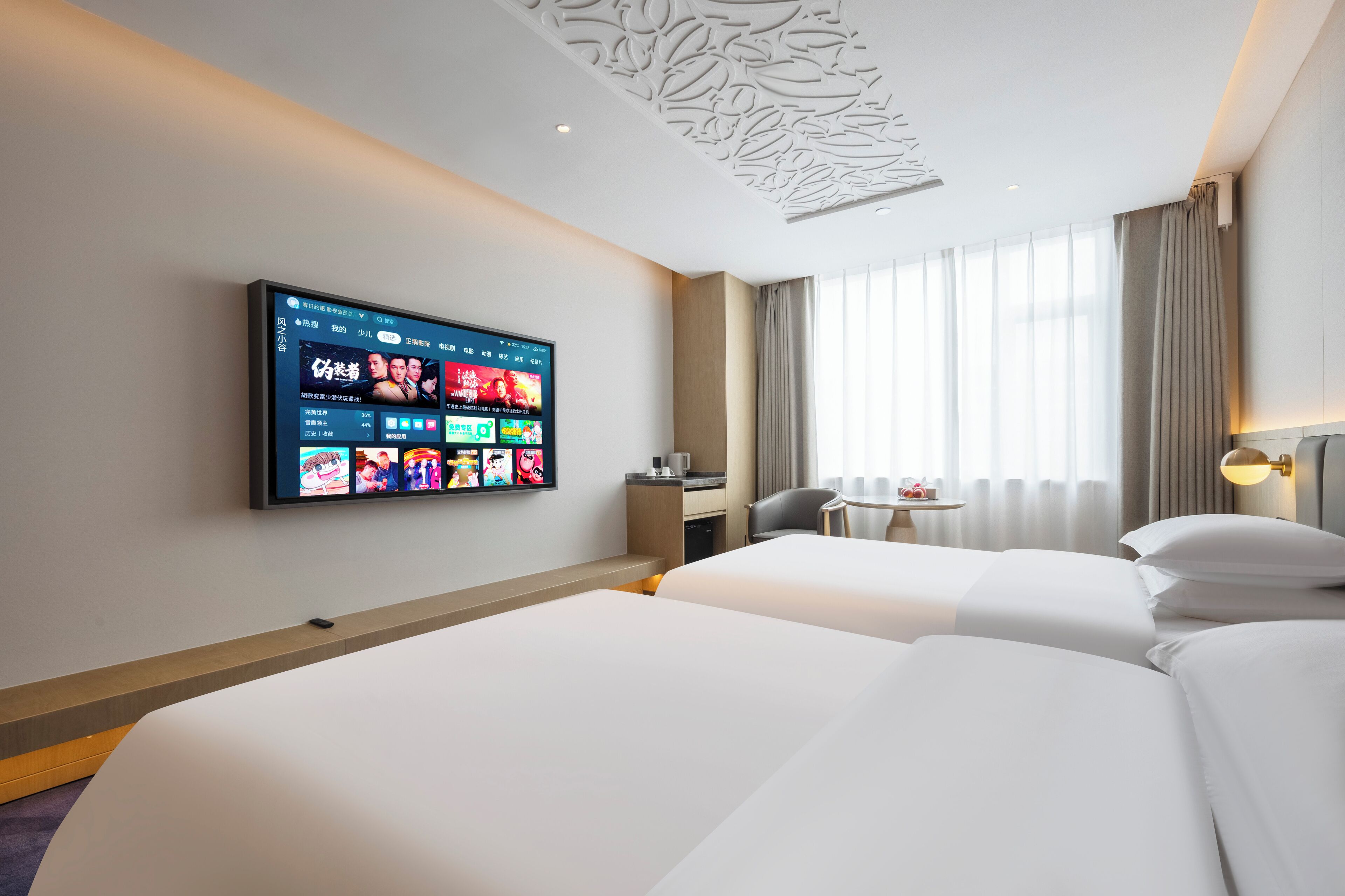 A hotel room with two beds, a desk, a chair, a TV mounted on the wall, and a window with curtains.
