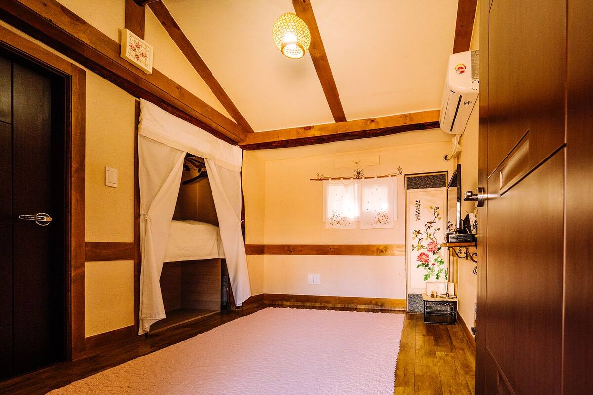 A traditional Japanese-style room with tatami flooring, a shoji screen door, a futon bed, and a wooden ceiling with exposed beams.