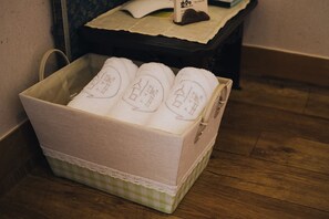 A storage box with towels, a tissue box, and a brown item on a wooden floor. - Hohomom Guesthouse (Jeonju)