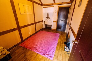 A small room with a wooden floor, a pink rug, a bed with a white canopy, a wooden door, and a wall-mounted picture. - Hohomom Guesthouse (Jeonju)