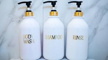 Three white bottles with gold and black pumps labeled "BODY WASH," "SHAMPOO," and "RINSE."