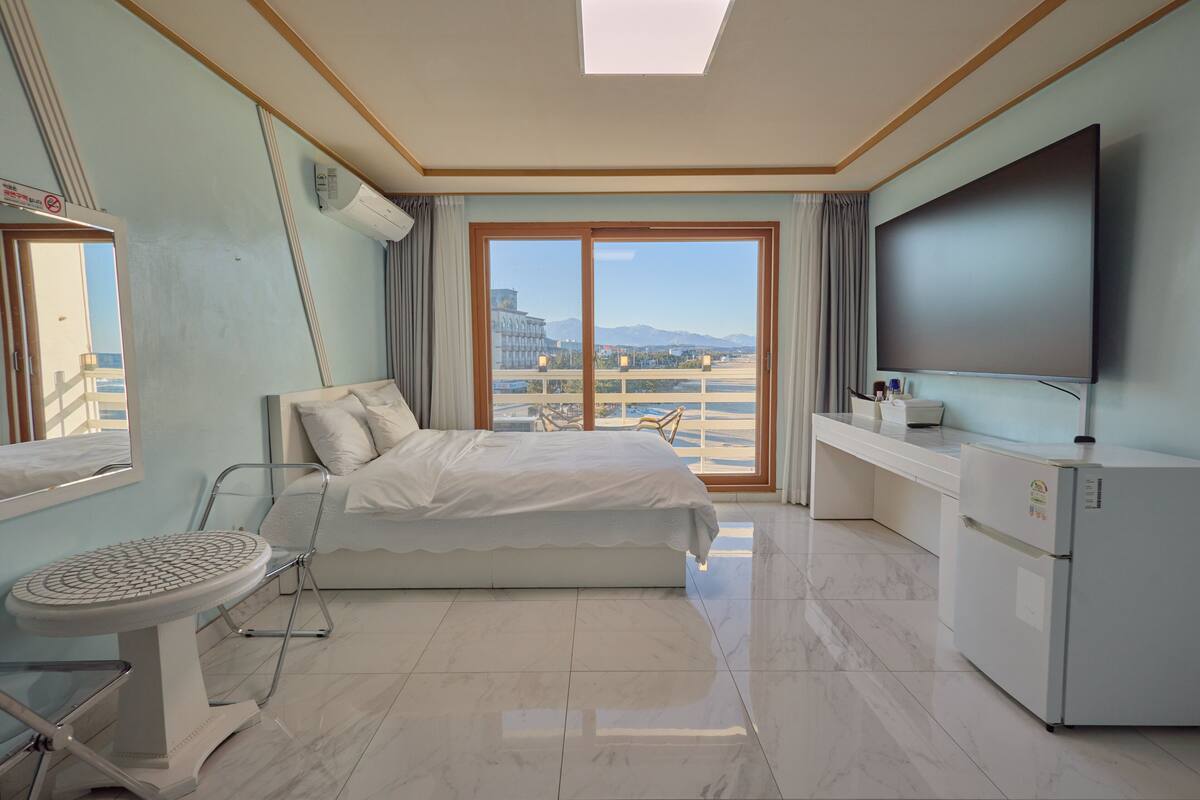 A hotel room with a bed, a TV, a desk, and a view of the city.
