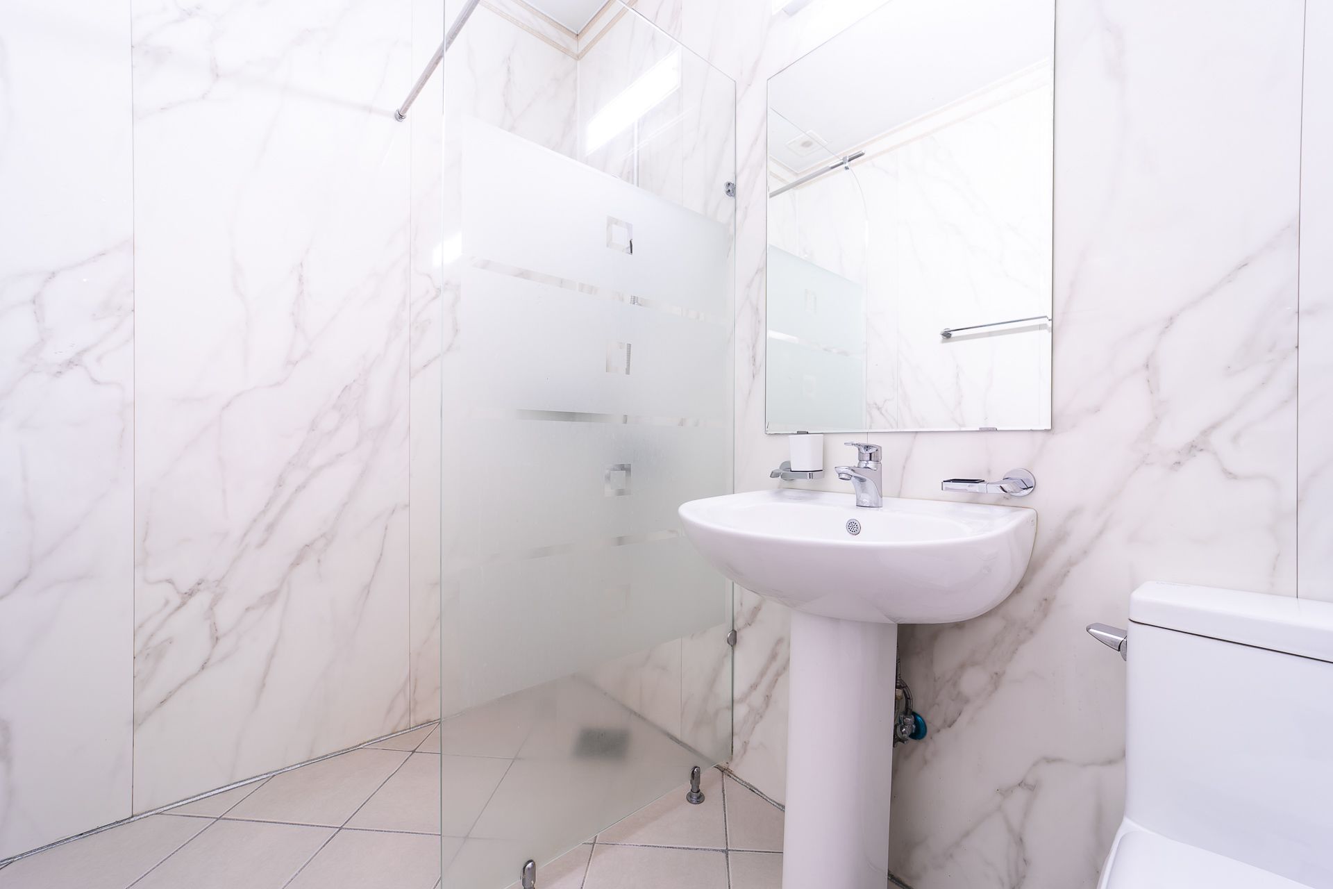A bathroom with a white sink, mirror, and toilet, featuring marble walls and floor tiles.