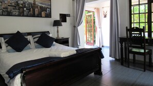Ein Schlafzimmer mit einem Bett, einem Nachttisch, einer Lampe, einem Sessel, einem Gemälde und einem Fenster mit Vorhängen.