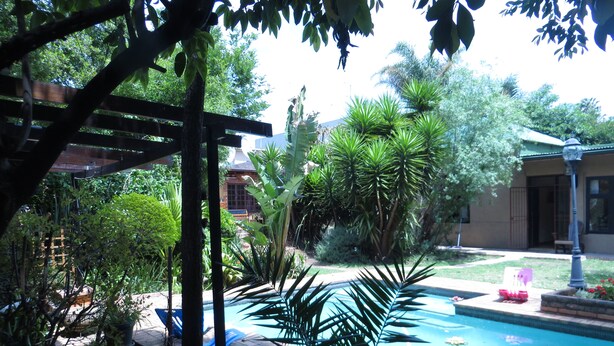 Ein Poolbereich mit einer Pergola, verschiedenen Pflanzen und einem Gebäude im Hintergrund.