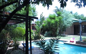 Ein Poolbereich mit einer Pergola, verschiedenen Pflanzen und einem Gebäude im Hintergrund.