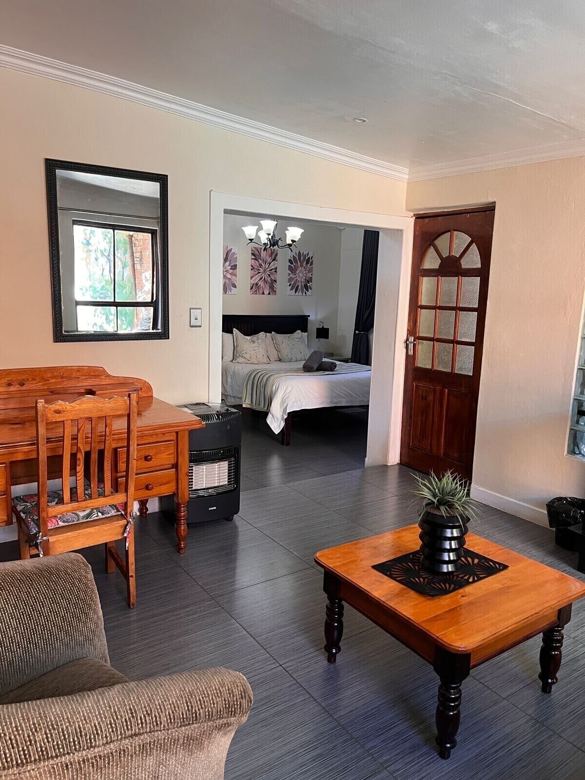 A room with a dining table, chairs, a sofa, a bed, a heater, and a potted plant.
