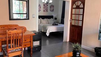 A room with a dining table, chairs, a sofa, a bed, a heater, and a potted plant.