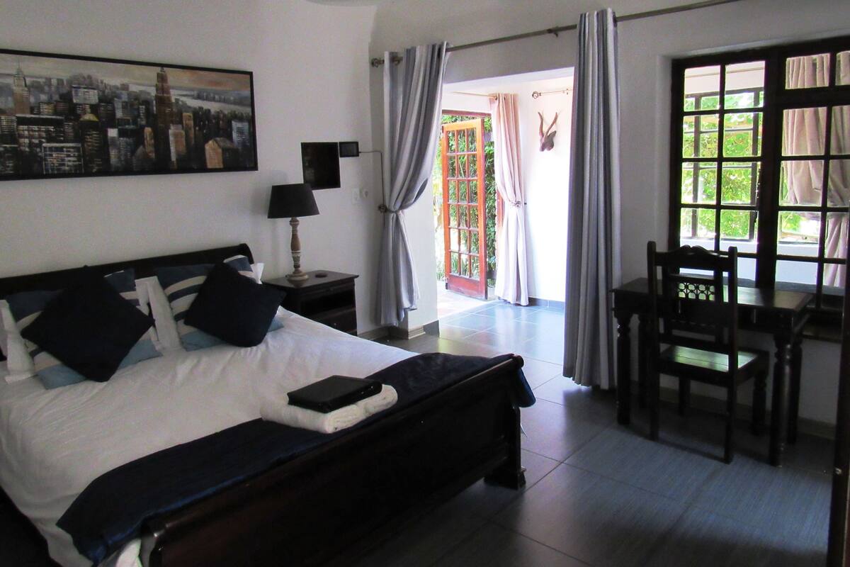 A hotel room with a bed, a desk, a chair, a lamp, and a large window.