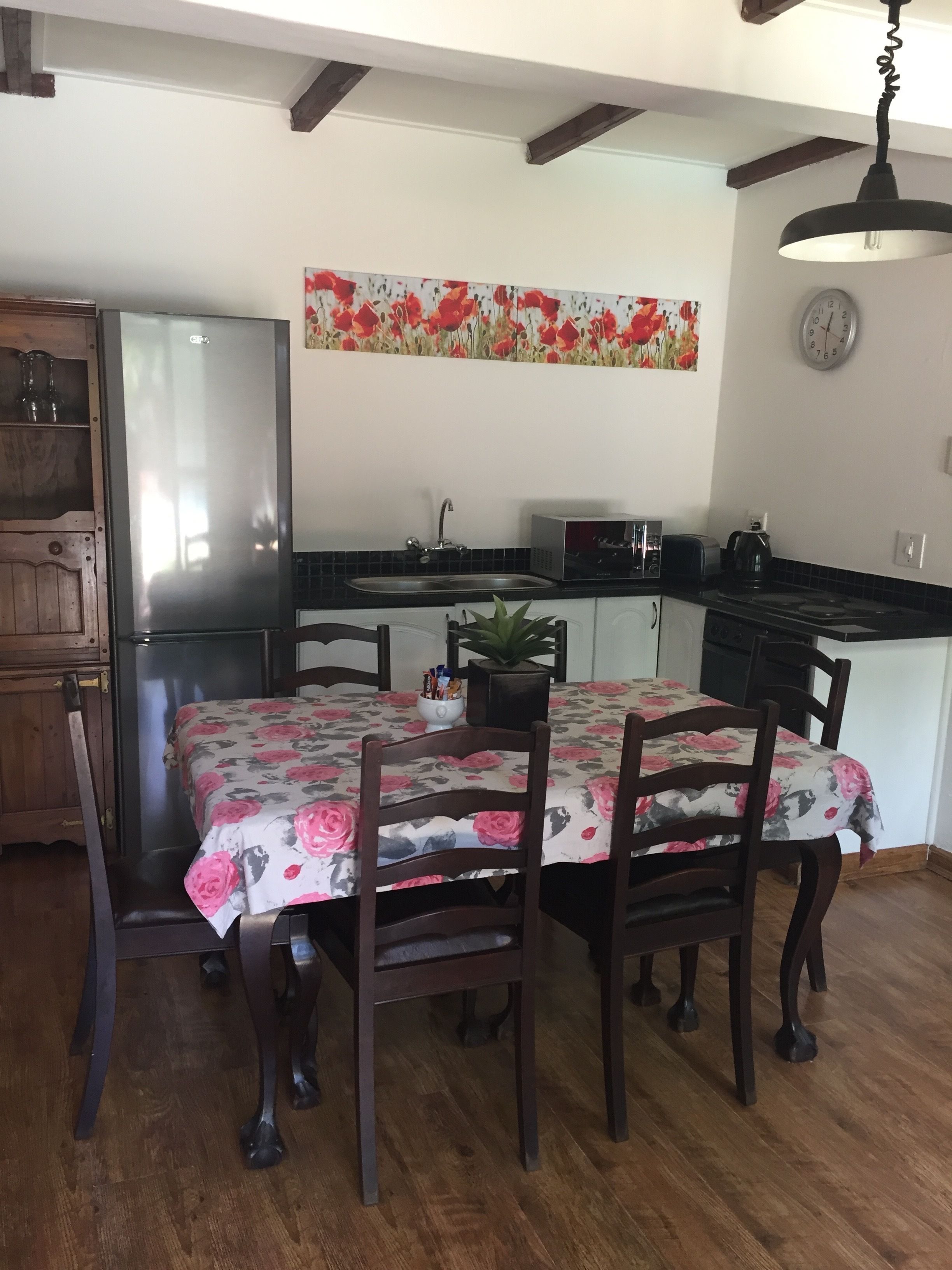 Un comedor con una mesa dispuesta para cuatro personas, rodeada de sillas de madera. Se observan una nevera y un microondas al fondo.