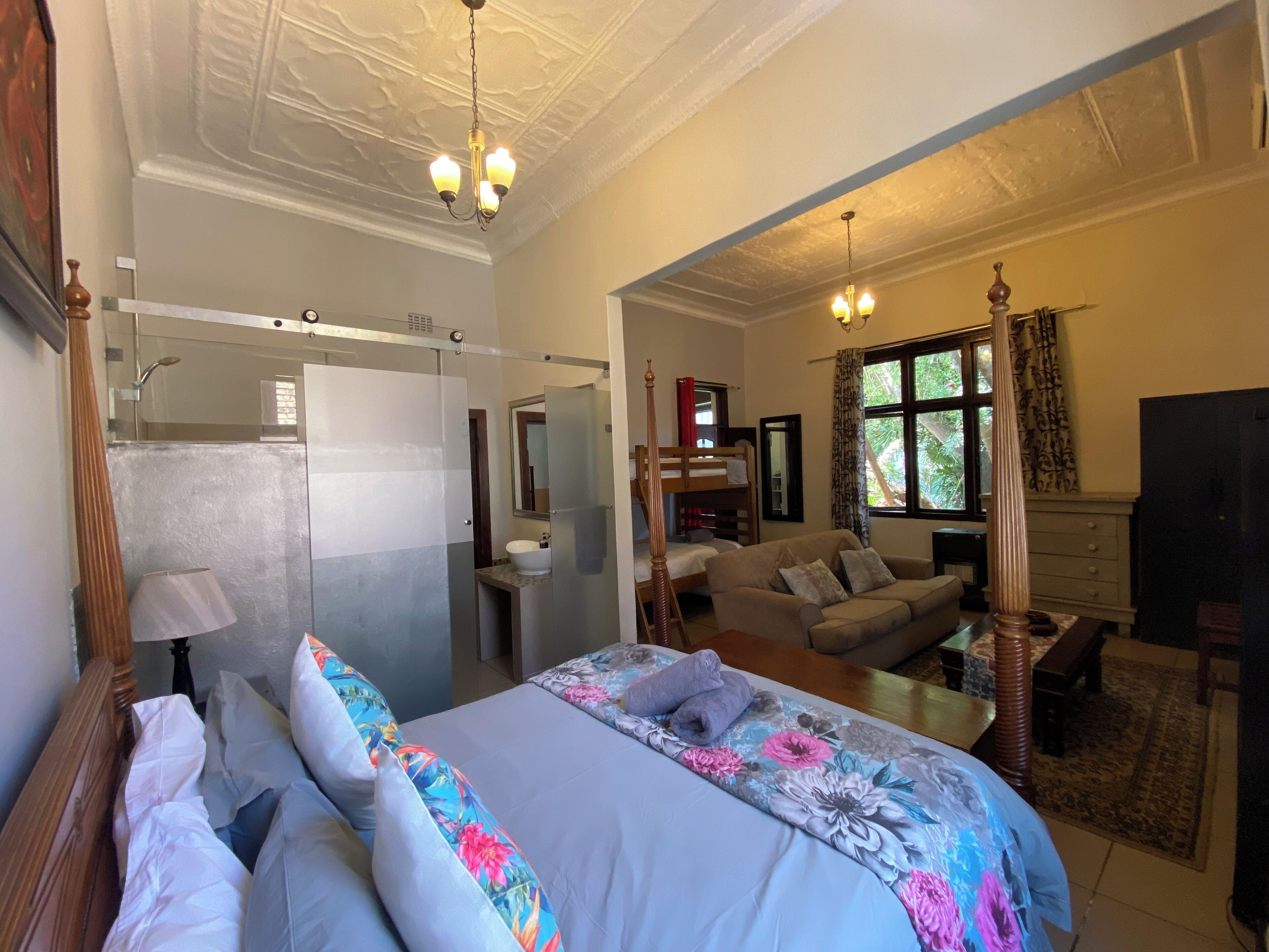 A hotel room with a bed, a sofa, a desk, a mirror, a window with curtains, and a door leading to a bathroom.