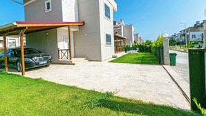 A modern two-story house with a covered patio, a car parked in the driveway, and a well-maintained lawn. - Paradise Town Villa Lisa (Serik)