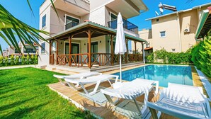 A modern two-story house with a swimming pool, a covered patio with lounge chairs, and a well-maintained lawn. - Paradise Town Villa Lisa (Serik)