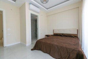 Une chambre dotée d’un grand lit, d’un climatiseur, d’une table de chevet et d’une porte donnant accès à une salle de bain.