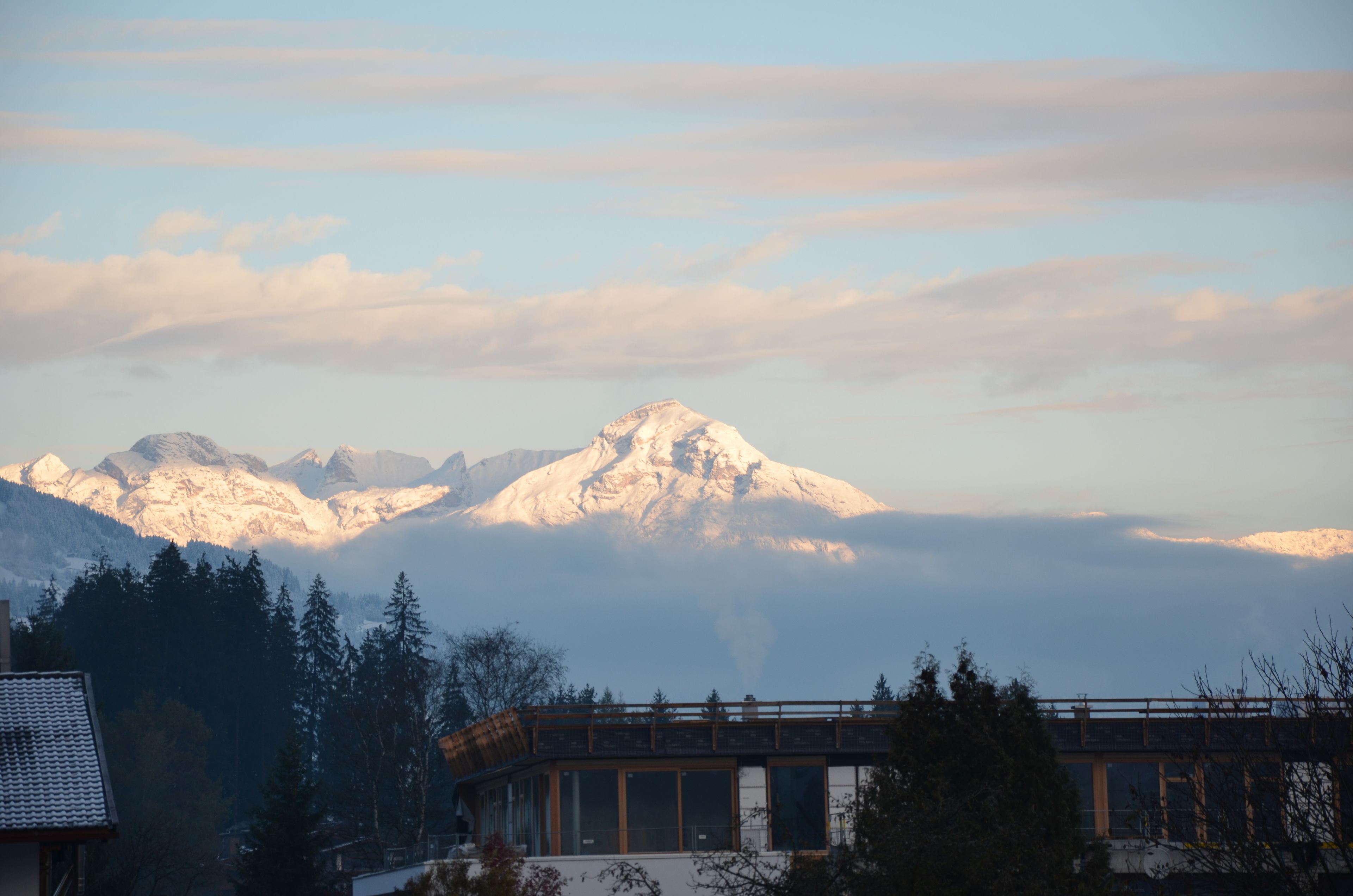 A mountain range with a prominent peak, a wooden bridge, and a building with large windows.