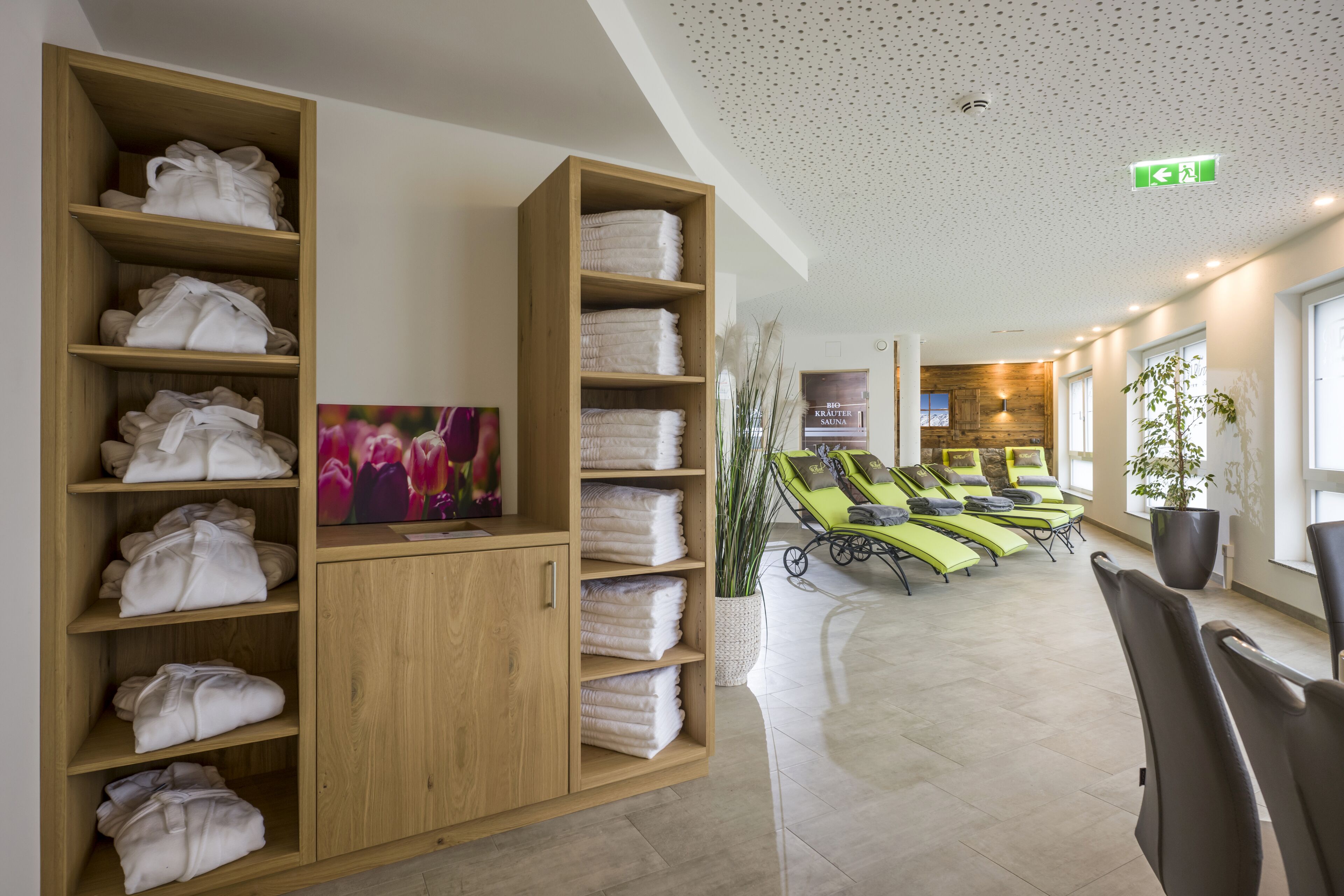 A hotel lobby with wooden shelves holding towels, a reception desk, and a seating area with sun loungers.