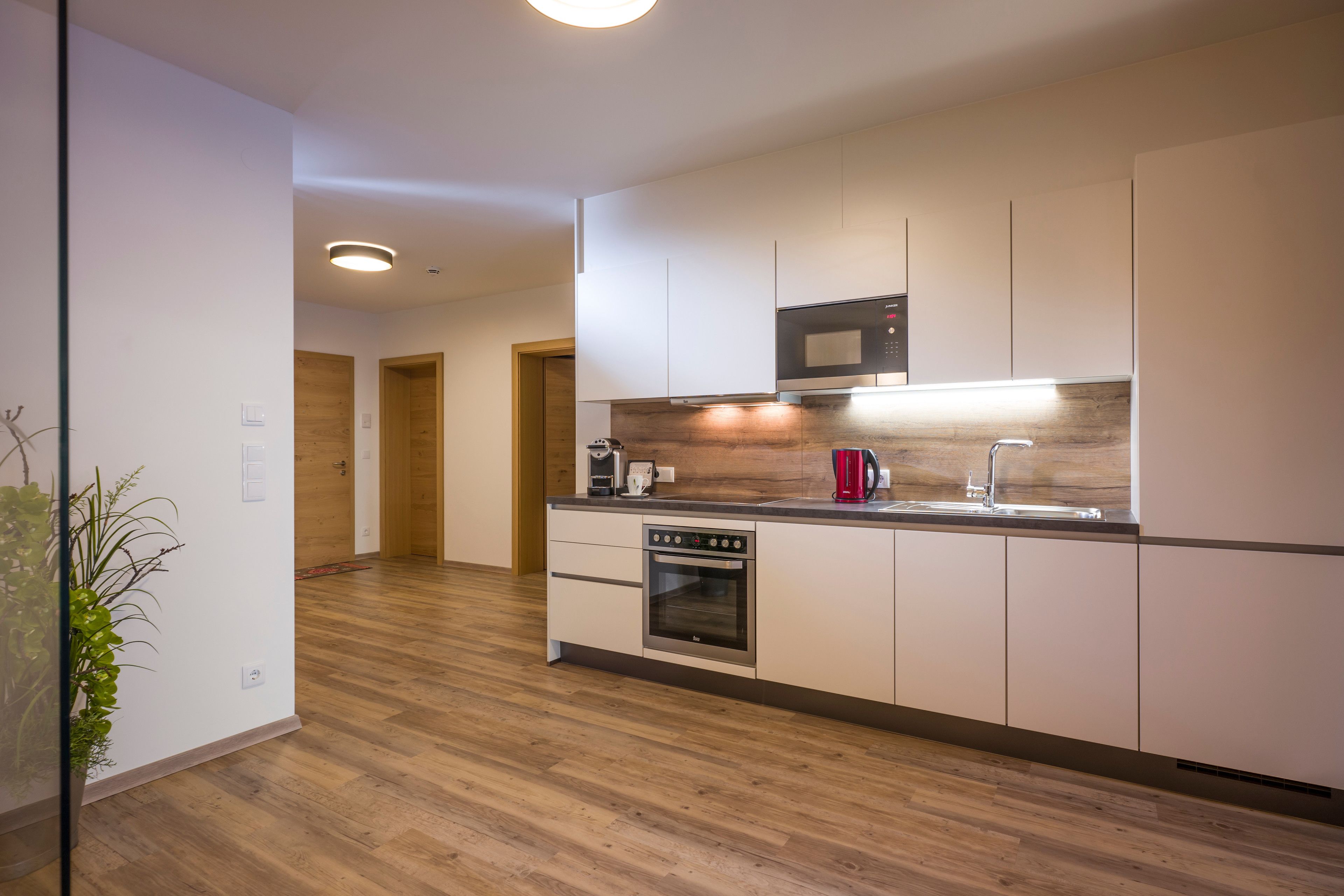A modern kitchen with white cabinetry, a built-in oven, a microwave, and a coffee maker.