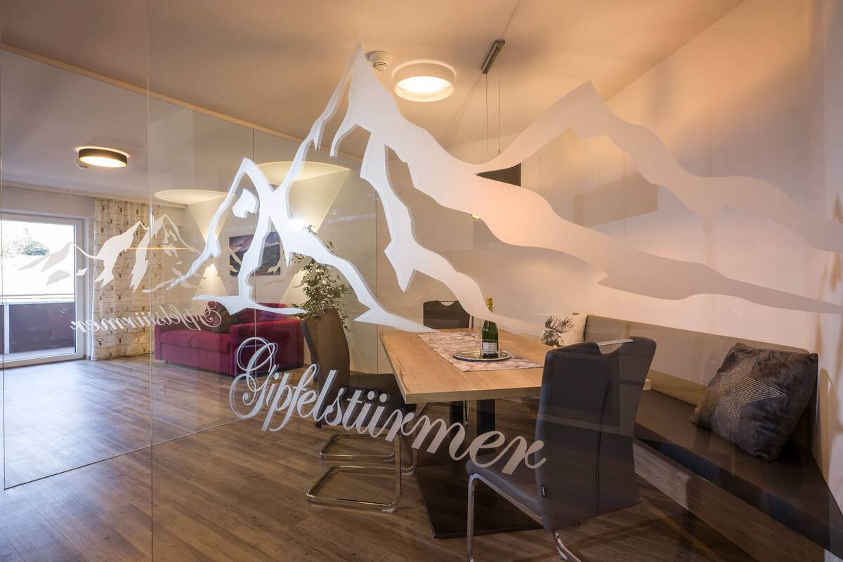 A modern dining area with a wooden table, chairs, and a glass partition with mountain designs.