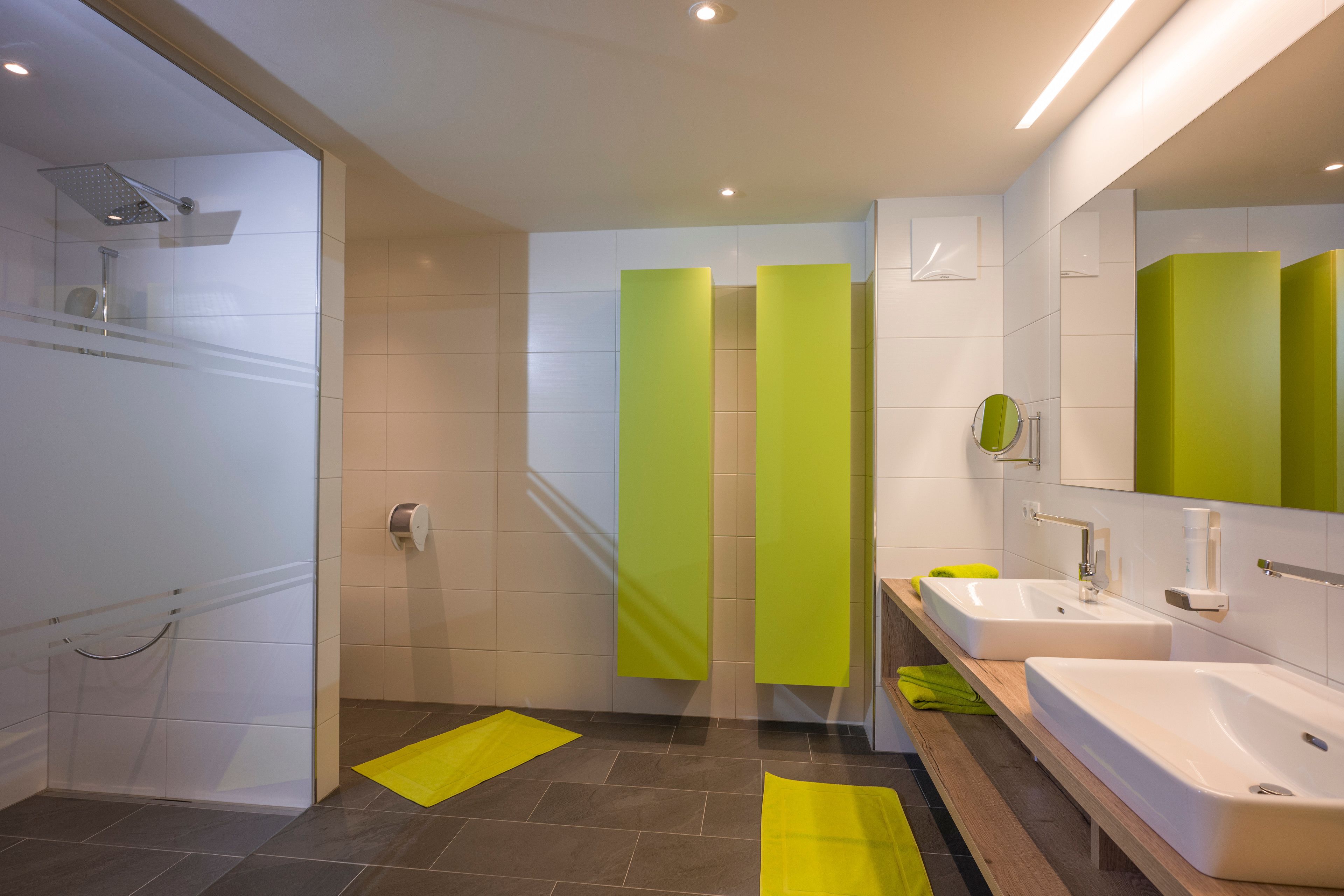 Un baño moderno con cabina de ducha de vidrio, dos lavamanos y un espejo.