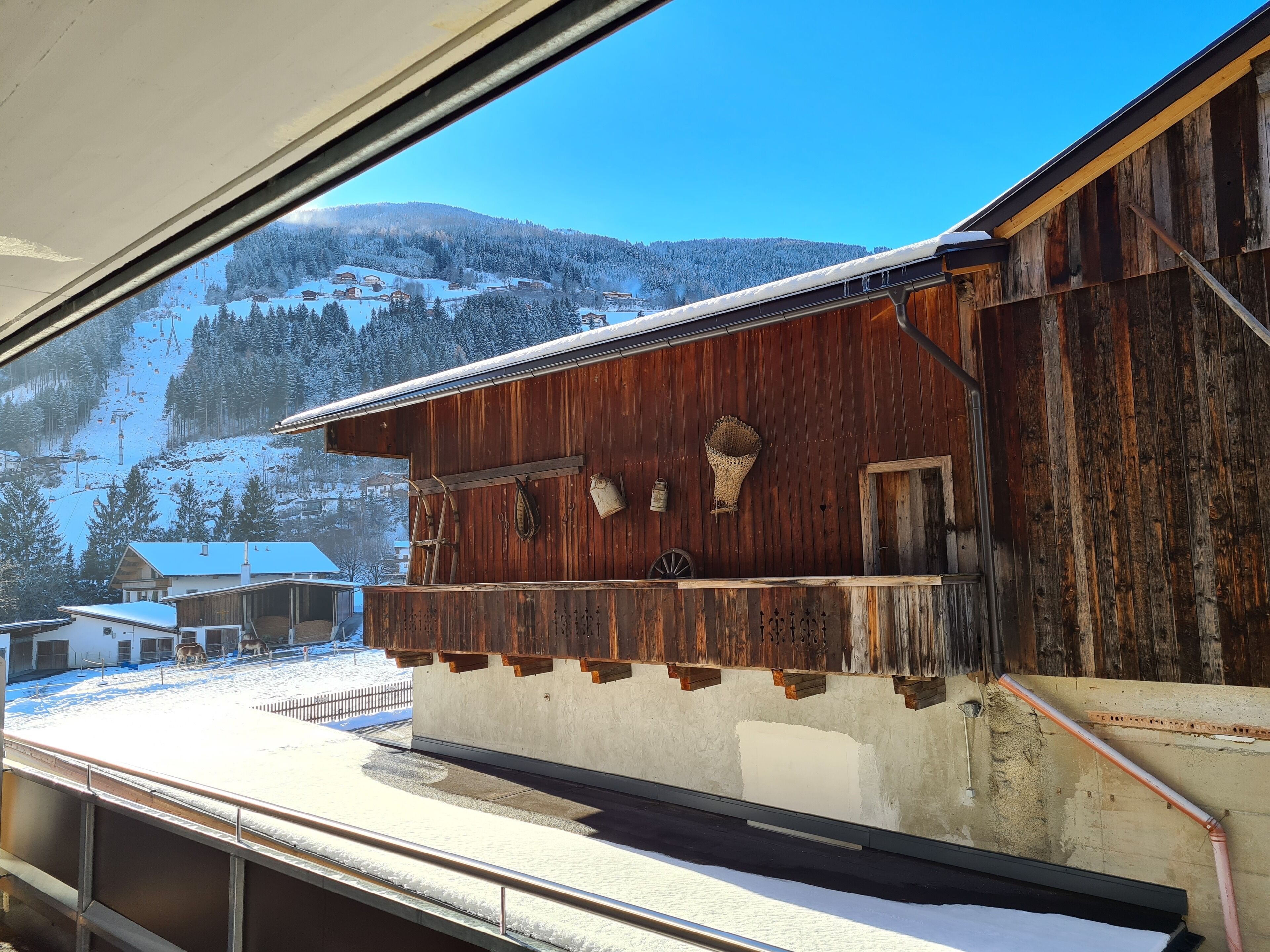 Un bâtiment rustique en bois, avec un toit enneigé, un balcon doté de balustrades et une vue sur un paysage montagneux couvert de neige.