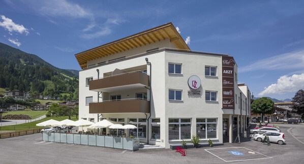 A multi-story building with a cafe on the ground floor, outdoor seating, and a parking area.
